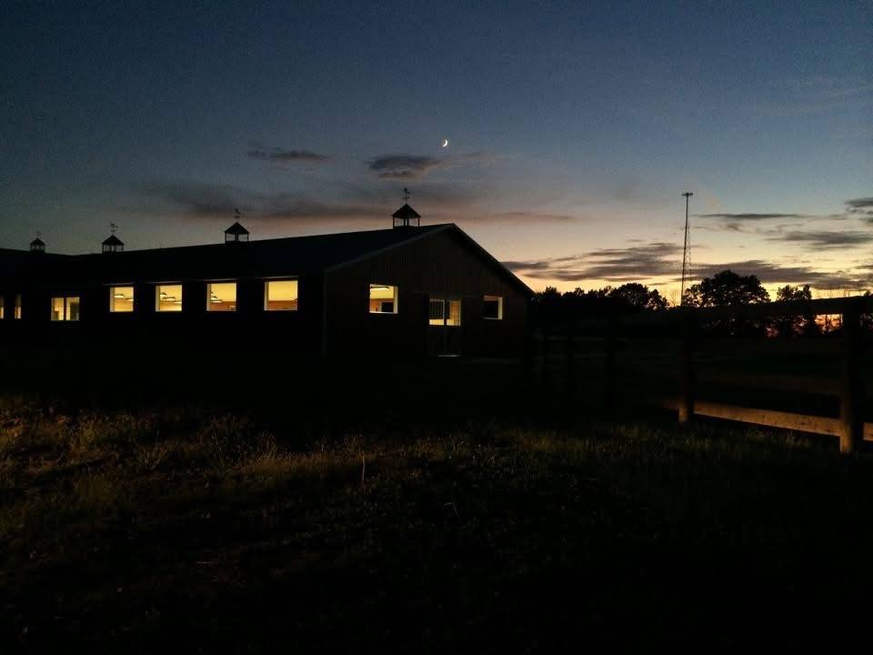 The barns lit at dusk under a crescent moon